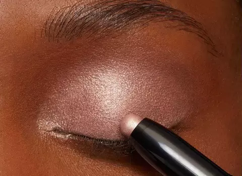 A woman applying a shimmery eye shadow to her eye lids.