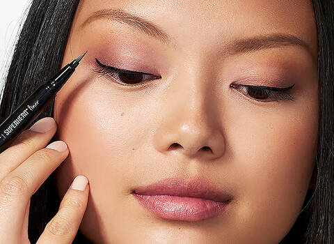A photo of a woman using liquid eye liner to make winged tips