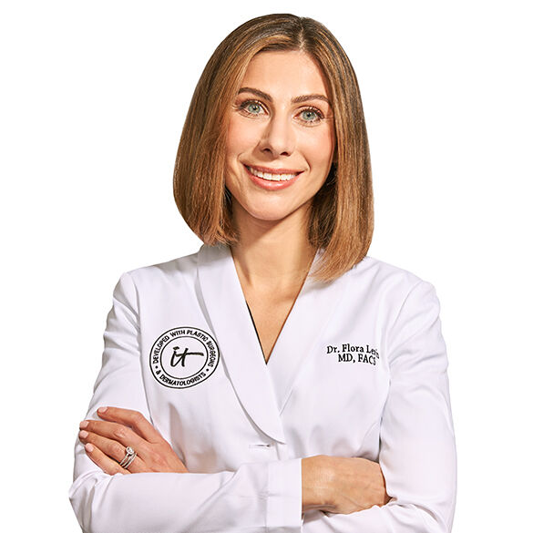 A headshot of IT Cosmetics advisor Dr. Flora Levin wearing a white doctor's coat with an embroidered IT Cosmetics seal.