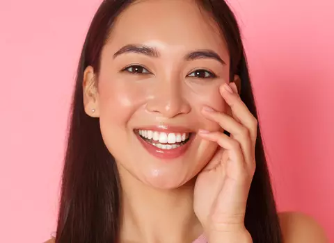 A person lightly touching their face, with a slight smile.