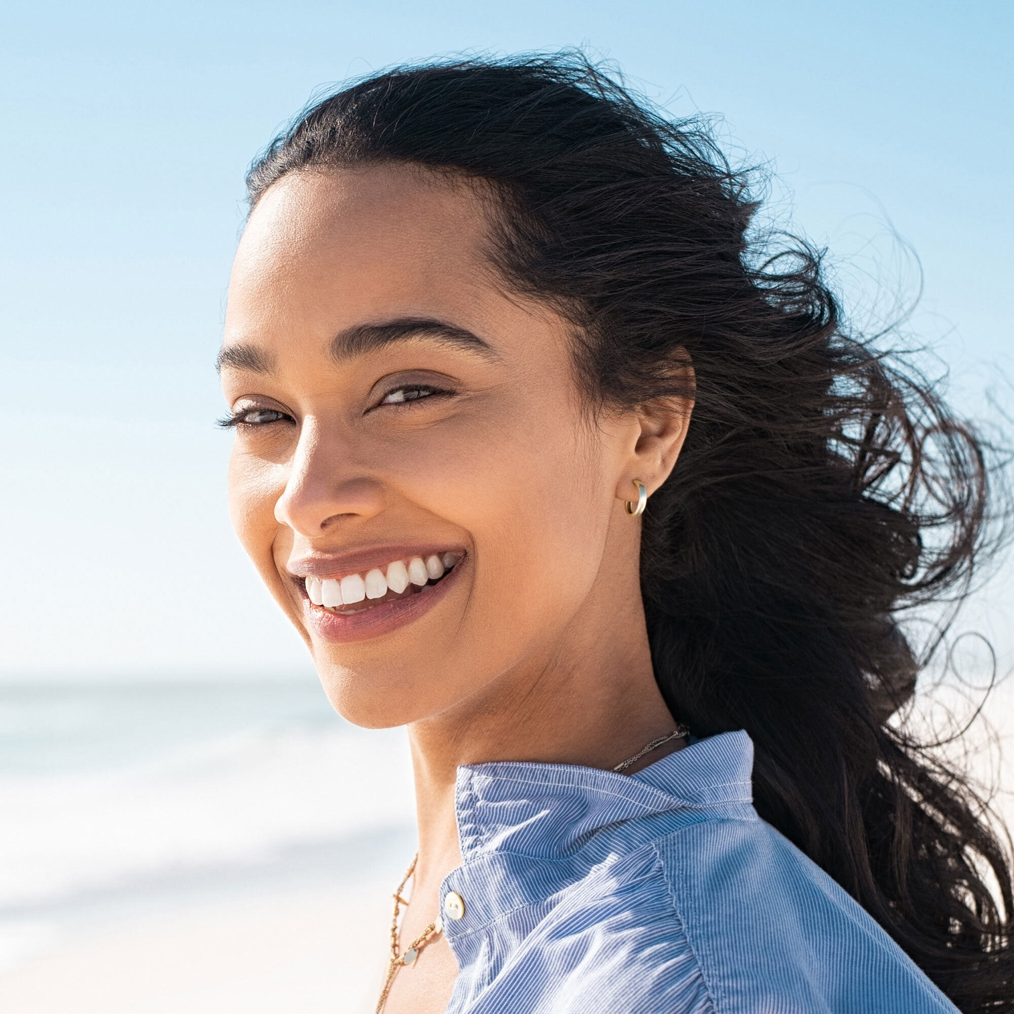 A photo of a smiling person standing on a beautiful beach.