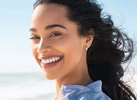 A photo of a smiling person standing on a beautiful beach.