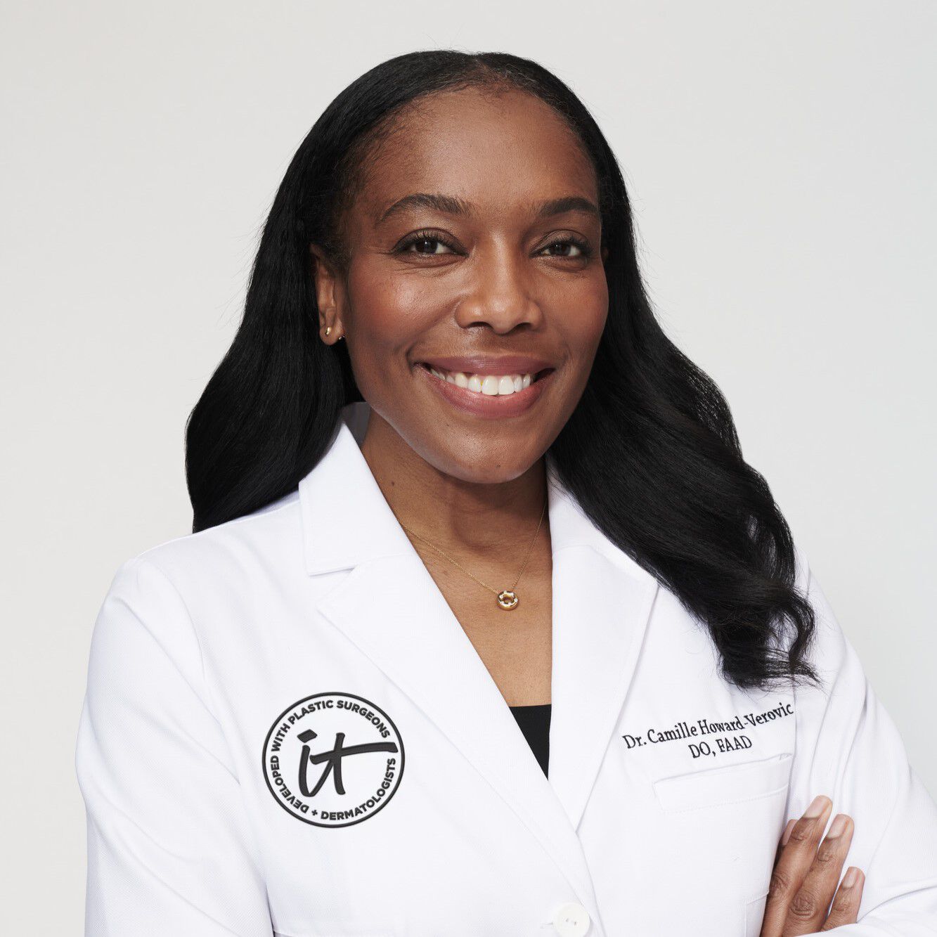 A headshot of IT Cosmetics advisor Dr. Camille Howard wearing a white doctor's coat with an embroidered IT Cosmetics seal.