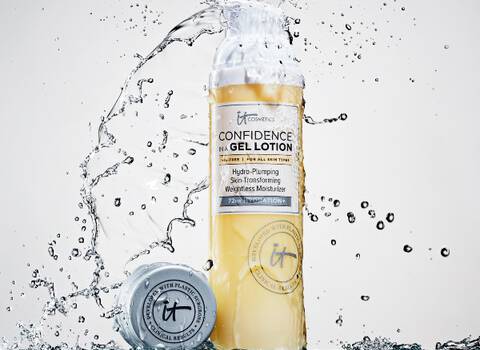 A bottle of IT Cosmetics Confidence In A Gel Lotion with the bottle cap next to it on a ledge being showered with water.