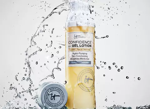 A bottle of IT Cosmetics Confidence In A Gel Lotion with the bottle cap next to it on a ledge being showered with water.
