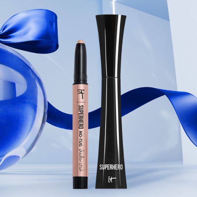 An IT Cosmetics Superhero No-Tug Waterproof Eyeshadow Stick in Silk Armor and Superhero Volumizing & Lengthening Mascara in Super Black on a blue background.