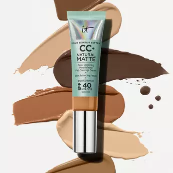 A tube of IT Cosmetics CC+ Cream Natural Matte Foundation with SPF 40 on a background of swipes of different foundation shades from light to deep and an IT Cosmetics seal in the top right corner.