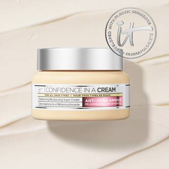 A jar of IT Cosmetics Confidence In A Cream on a background of light-colored cream and an IT seal in the top right corner.
