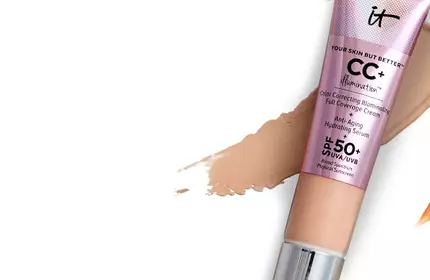 A close-up of a tube of IT Cosmetics CC+ Color Correcting Illuminating Full Coverage Cream SPF 50+ on a white background and a swipe of foundation.