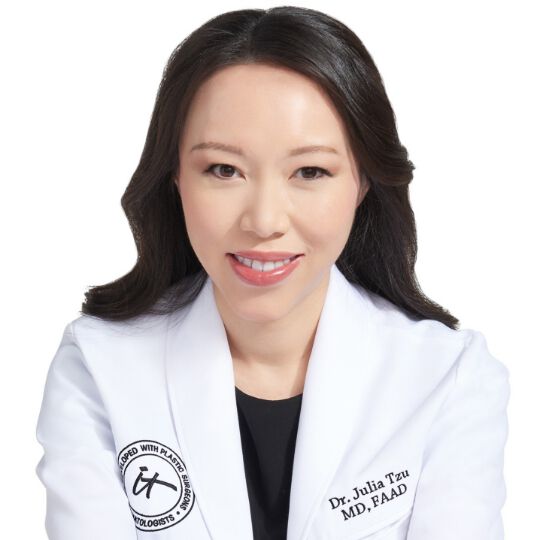 A headshot of IT Cosmetics advisor Dr. Julia Tzu wearing a white doctor's coat with an embroidered IT Cosmetics seal.