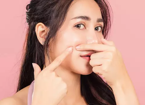 A photo of a woman pointing out a blemish on her face