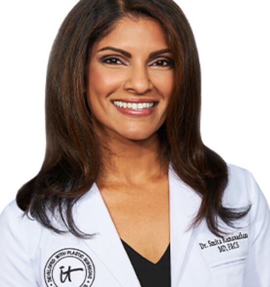 A headshot of IT Cosmetics advisor Dr. Smita R. Ramanadham wearing a white doctor's coat with an embroidered IT Cosmetics seal.