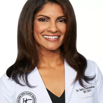 A headshot of IT Cosmetics advisor Dr. Smita R. Ramanadham wearing a white doctor's coat with an embroidered IT Cosmetics seal.