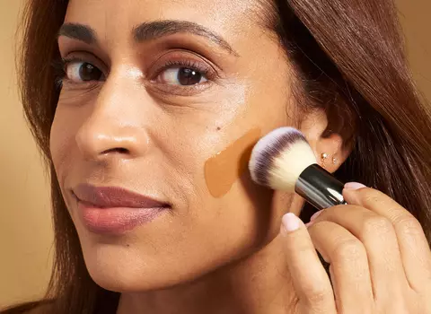 A person using a makeup brush to apply foundation to their face.