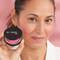 Woman with faint smile and dark hair holding up Bye Bye Pores Blush