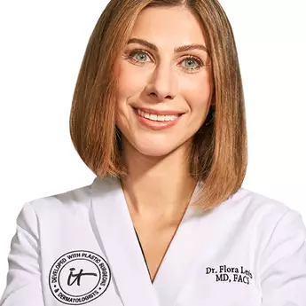 A headshot of IT Cosmetics advisor Dr. Flora Levin wearing a white doctor's coat with an embroidered IT Cosmetics seal.