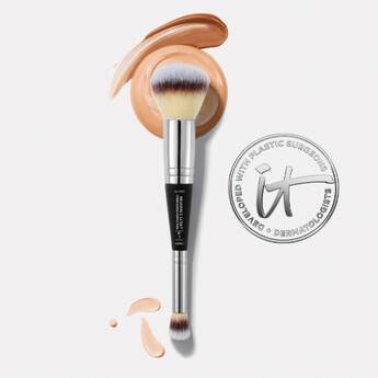 A double-sided IT Cosmetics makeup brush on a white background and swipes of complexion makeup next to an IT Cosmetics seal.