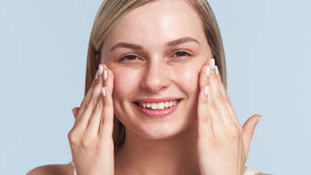 Smiling woman applying face cream with both hands